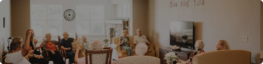 A gathering of individuals in chairs, interacting with one another in a comfortable room setting.